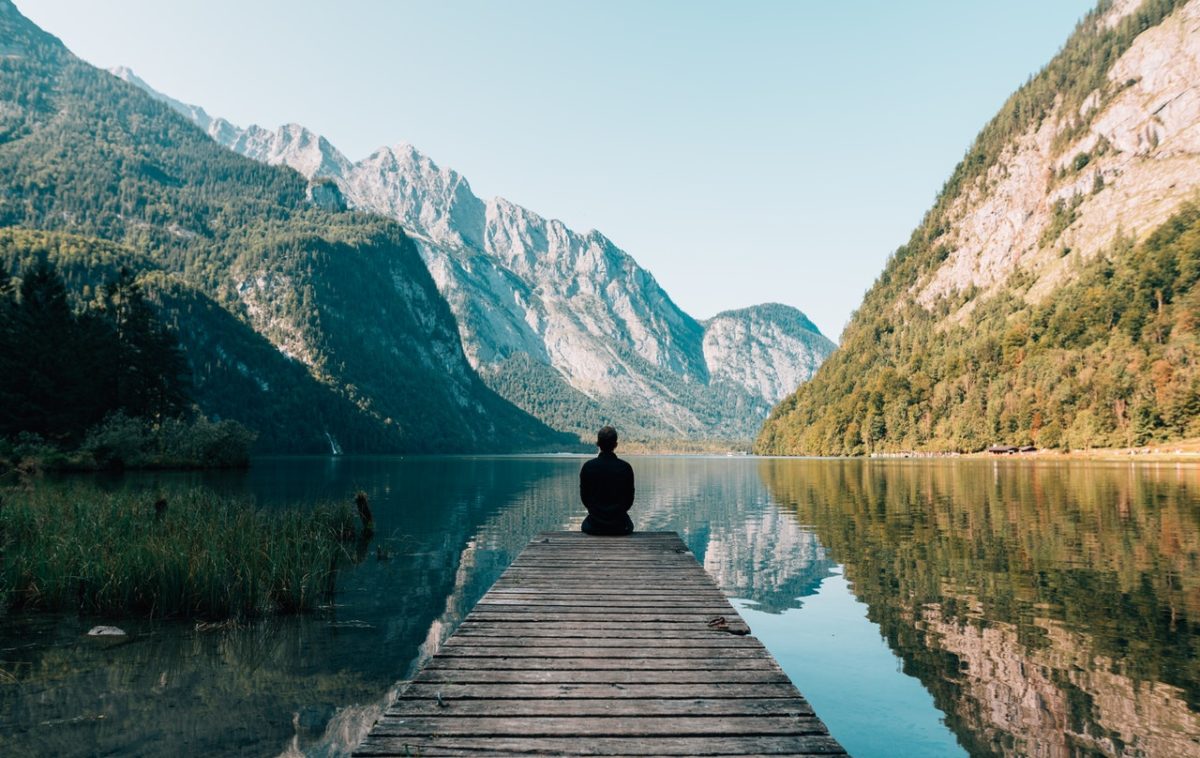 a person sitting on a dock over a lake with mountains in the background